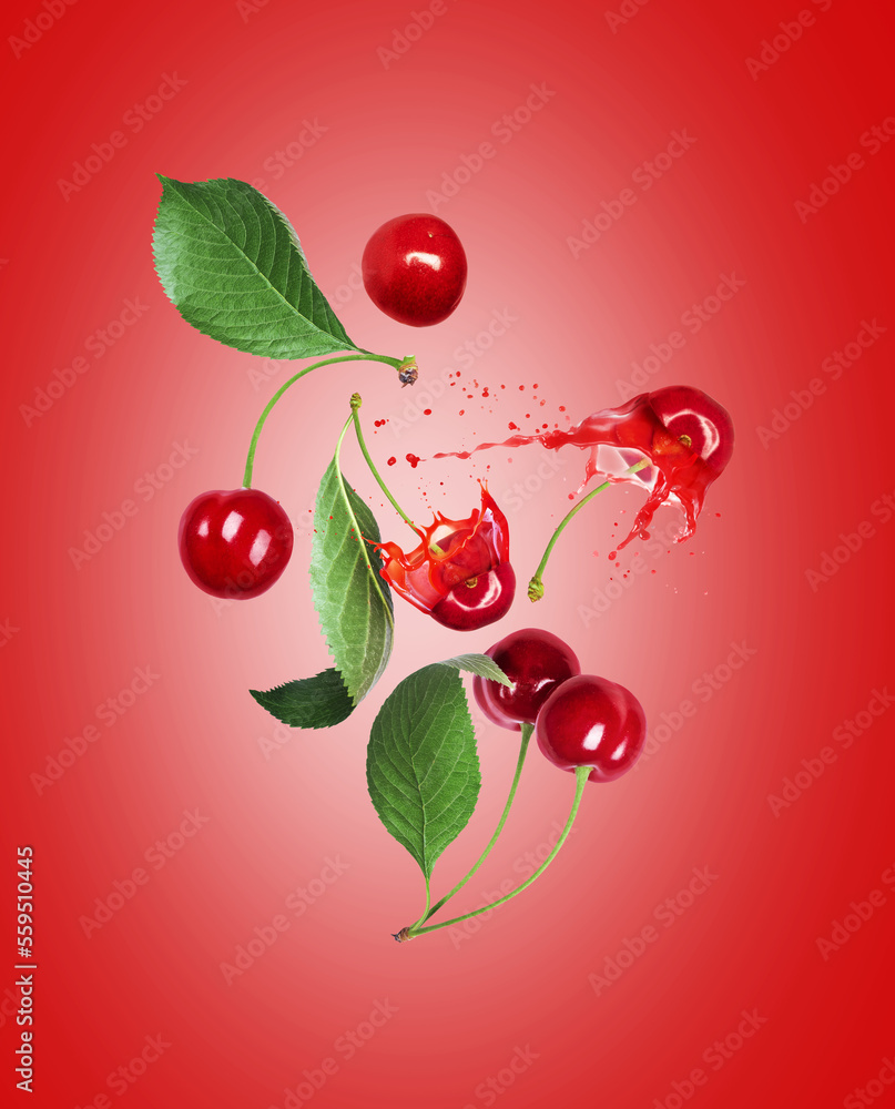 Whole and sliced cherries with juice splashes in the air on a red background