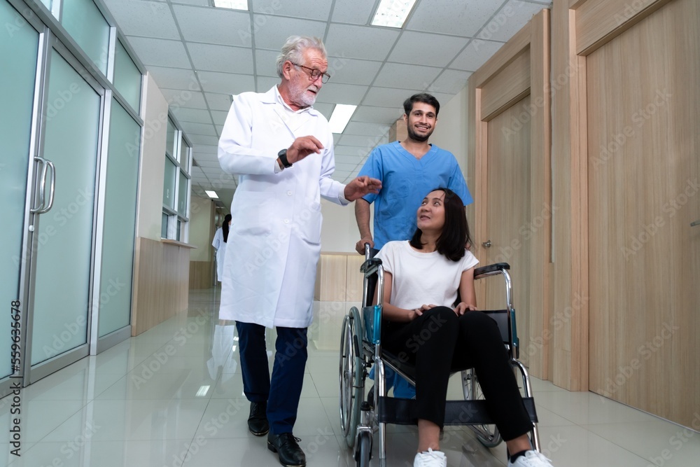 Doctor and male nurse transport a female patient in a wheelchair along sterile hospital corridor. He