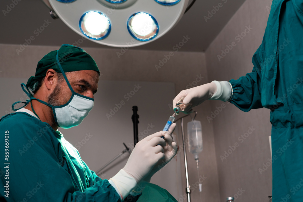 Surgeon fill syringe from medical vial for surgical procedure at sterile operation room with assista