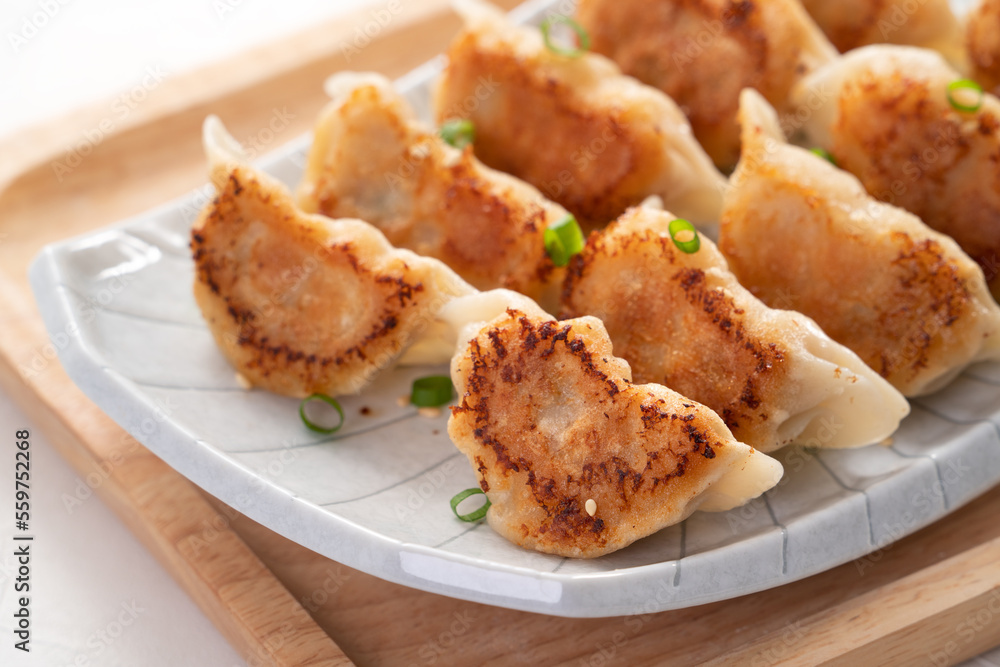 Pan-fried gyoza dumpling jiaozi in a plate with soy sauce on white table background.