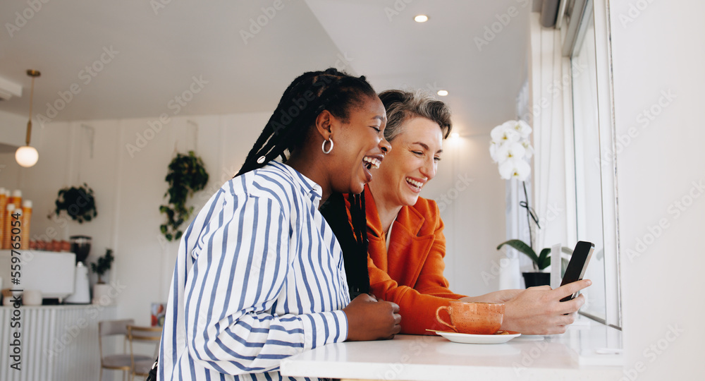 Smiling business women video calling their colleagues on a smartphone in a cafe