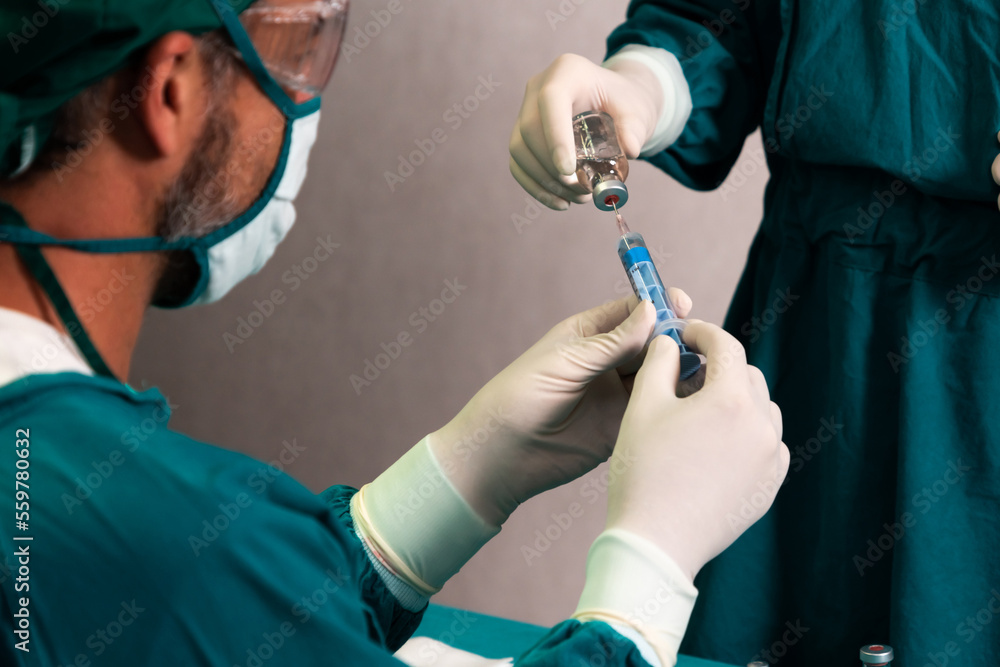 Surgeon fill syringe from medical vial for surgical procedure at sterile operation room with assista