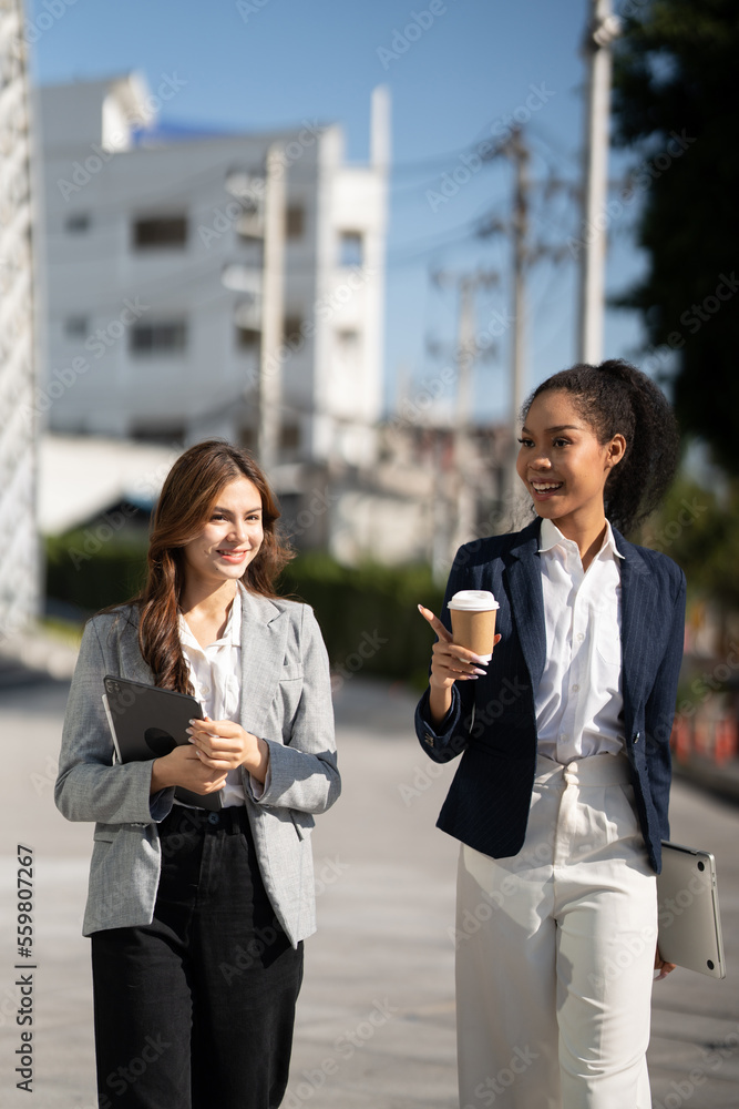 Two Asian businesswomen discussing business information while standing outside the office.