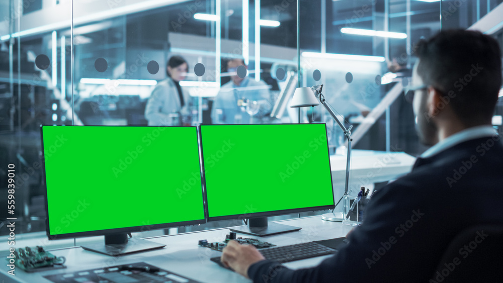 Industrial Engineer Working on a Desktop Computer with Two Green Screen Chromakey Display Screens in