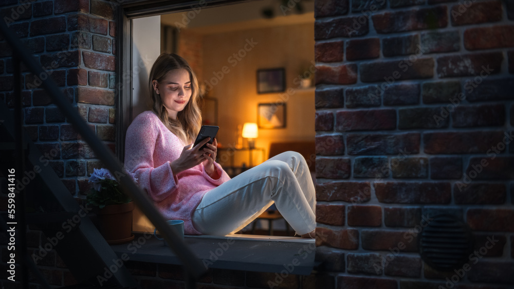 White Woman Using a Smartphone while Sitting on a Windowsill in Brooklyn Style Brownstone House. You