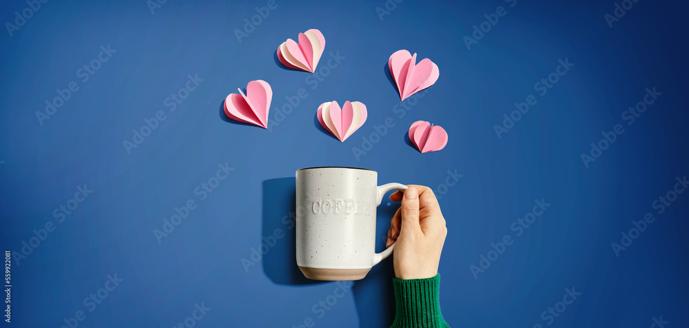 Female hand holding a mug with paper craft hearts - flat lay