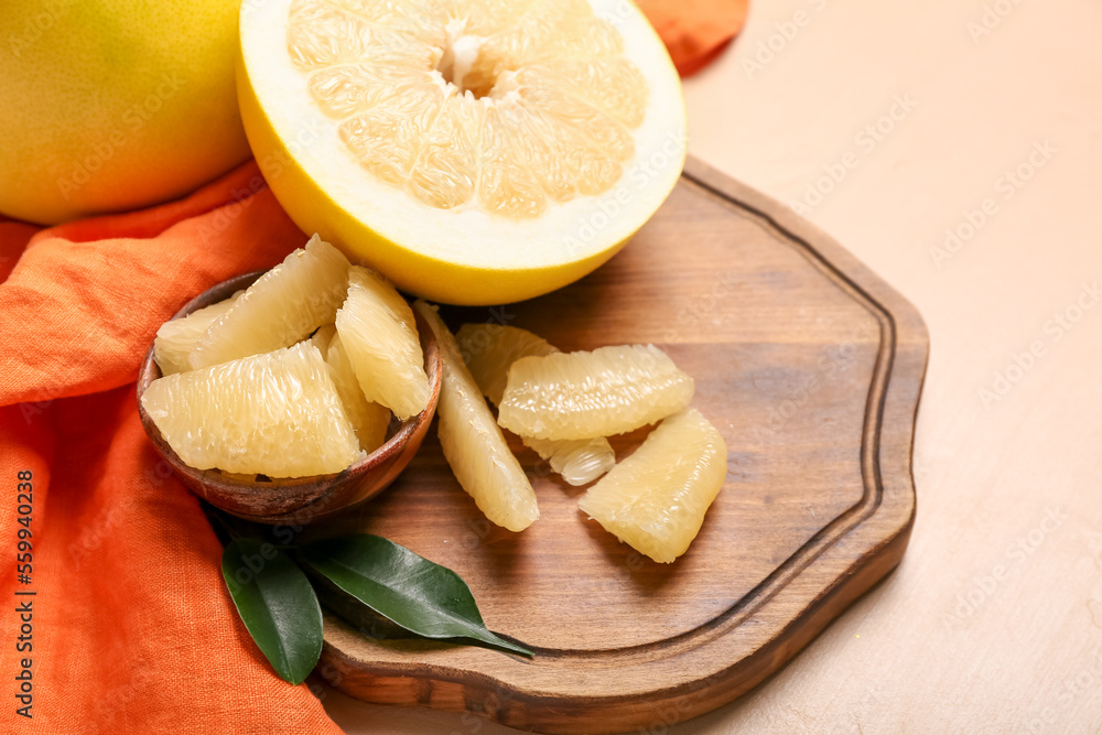 Wooden board with pomelo fruit on beige background, closeup