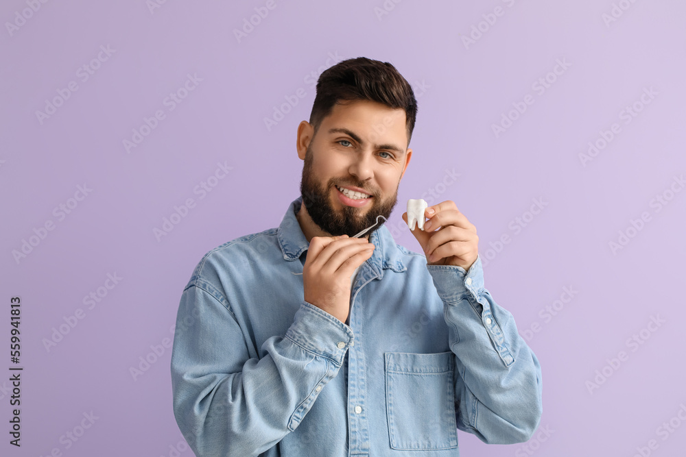 Young man with plastic tooth and dental tool on violet background