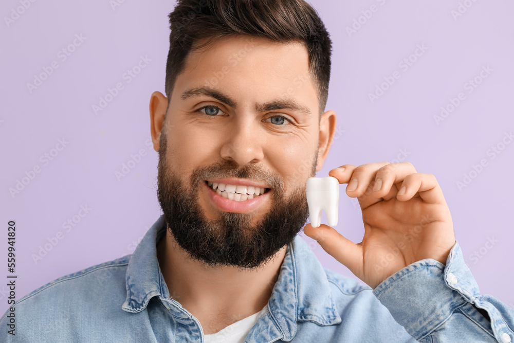 Young man with plastic tooth on violet background, closeup