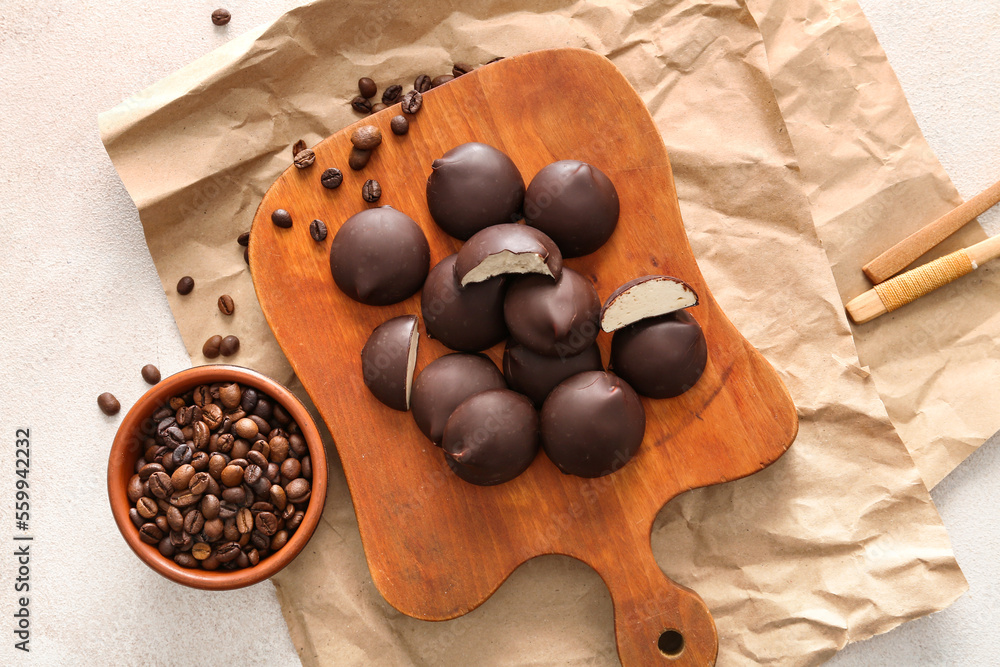 Cutting board with tasty birds milk candies and coffee beans on light background