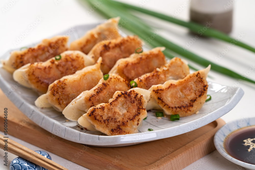 Pan-fried gyoza dumpling jiaozi in a plate with soy sauce on white table background.