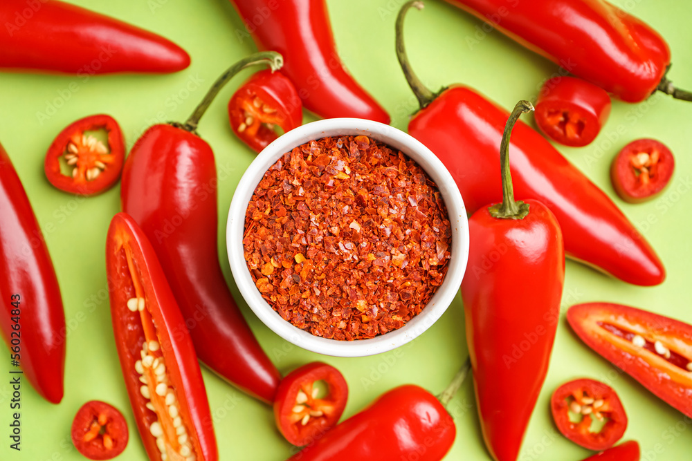 Bowl of chipotle chili flakes and fresh jalapeno peppers on green background