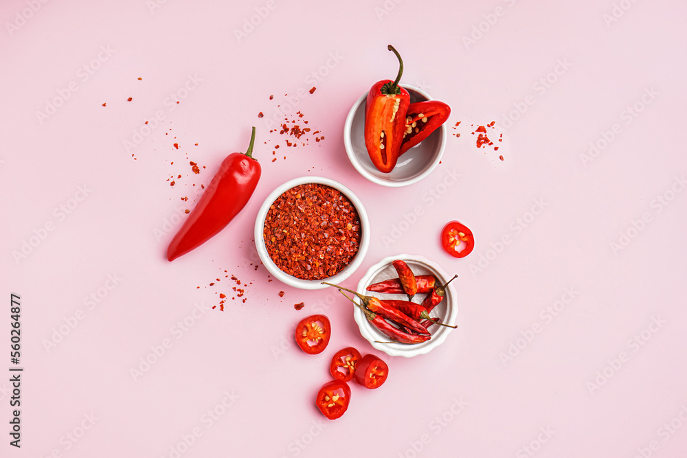 Bowls of chipotle chili flakes, fresh and dried jalapeno peppers on pink background