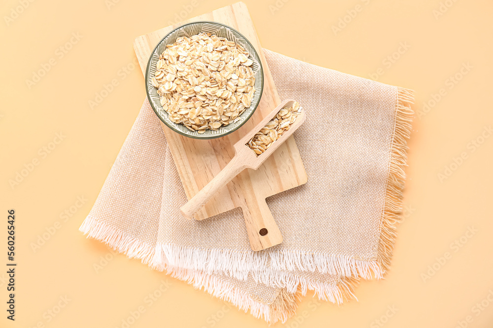 Wooden board with bowl and scoop of raw oatmeal on color background