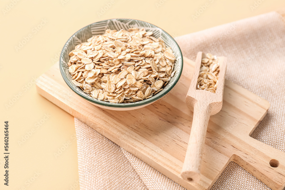 Wooden board with bowl and scoop of raw oatmeal on color background, closeup