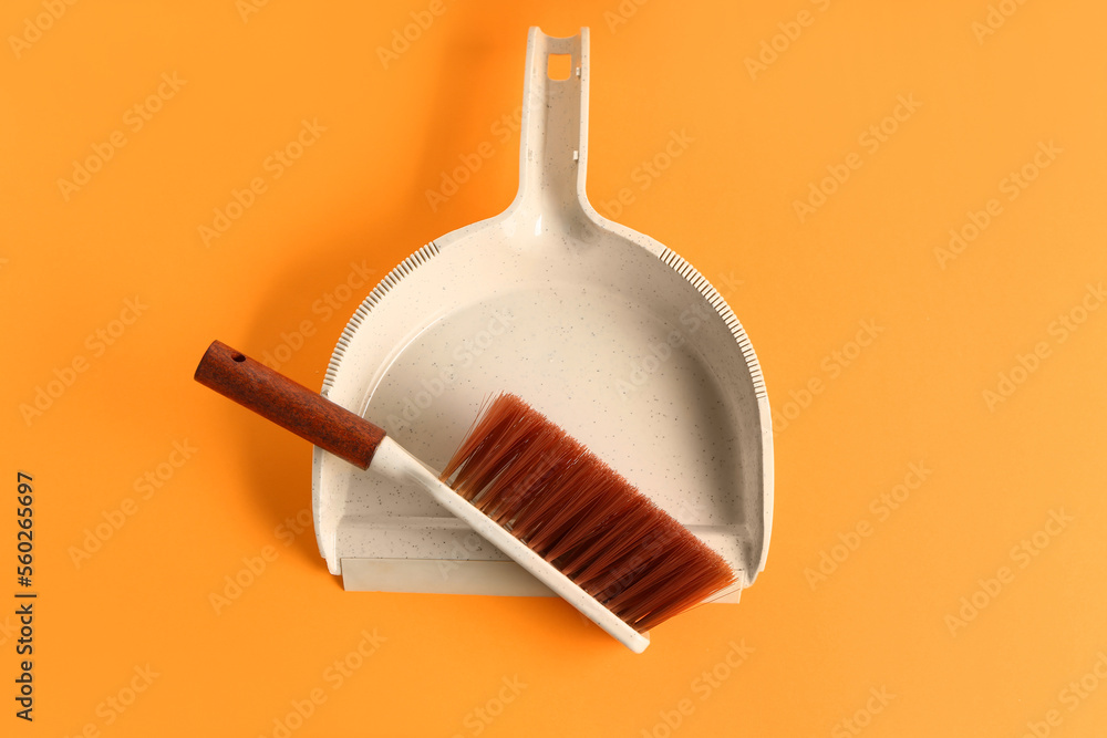 Dustpan and brush on orange background