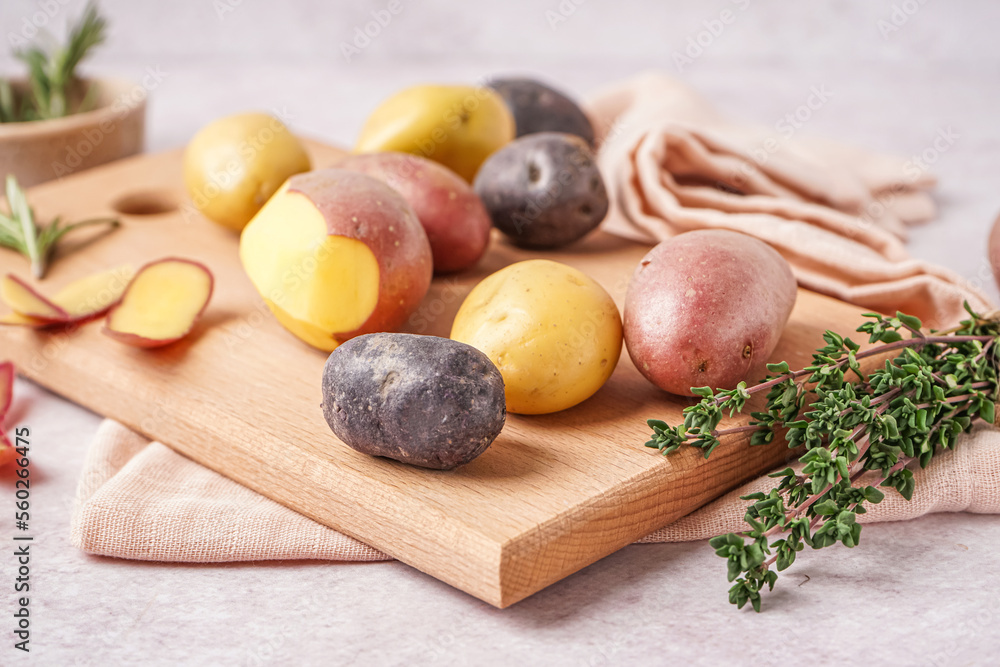 Wooden board with different raw potatoes and thyme on table, closeup