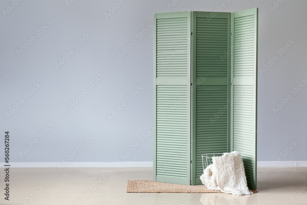 Basket with plaid and green folding screen near grey wall