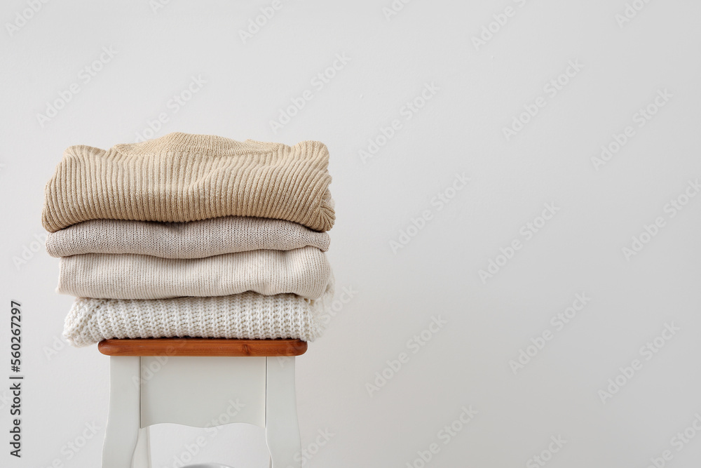 Folded knitted sweaters on table near light wall