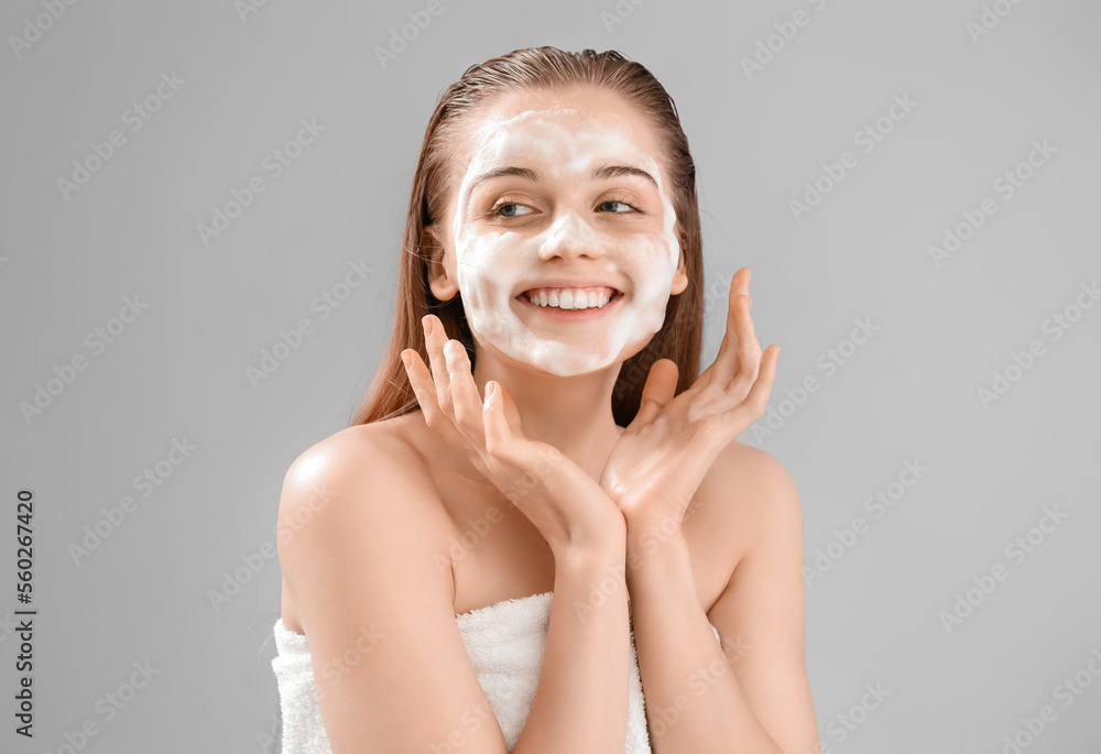 Beautiful young woman with soap foam on face against grey background