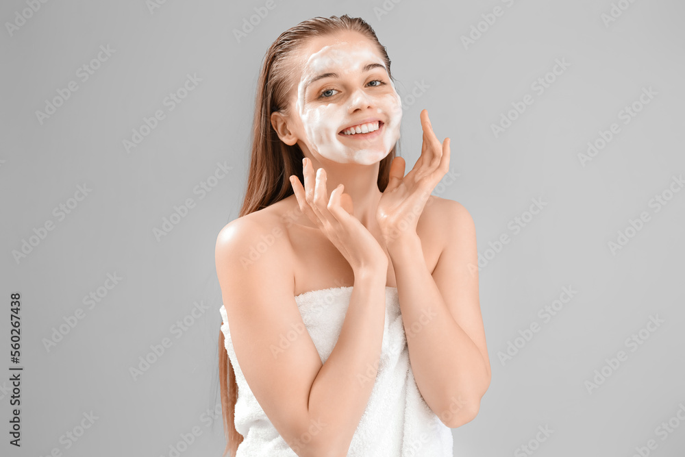 Beautiful young woman with soap foam on face against grey background