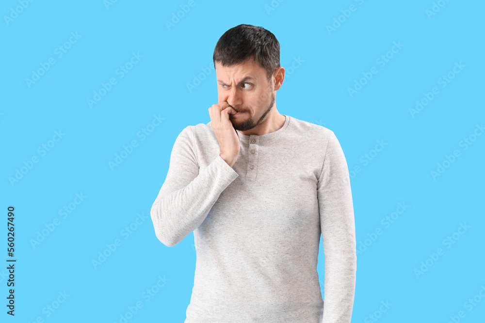 Handsome man biting nails on blue background