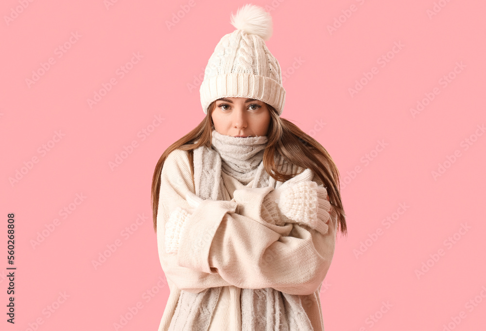 Frozen young woman in winter clothes on pink background