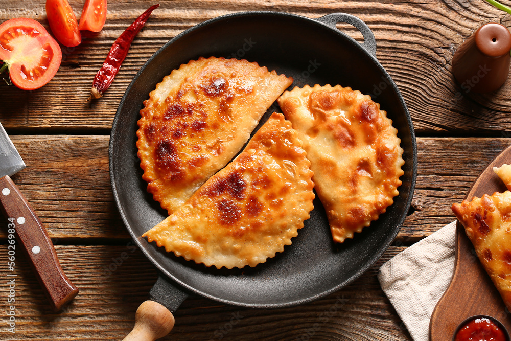 Frying pan with tasty chebureks on wooden background