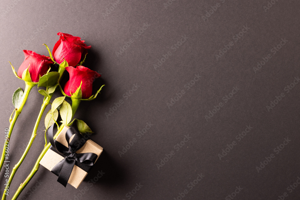 Image of close up of red roses and present and copy space on black background