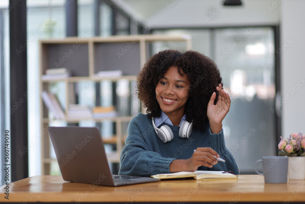 Portrait of young african woman working with laptop and reading books preparing for exams at her hom