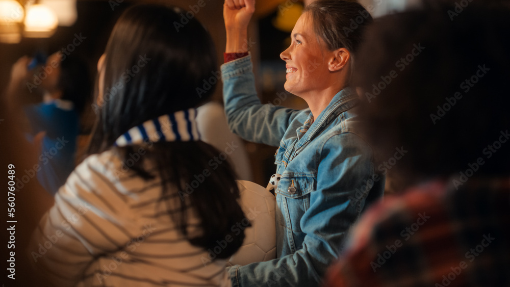 瓦特一家酒吧里，一位身穿牛仔外套的兴奋年轻女性站在一群体育迷中间的肖像