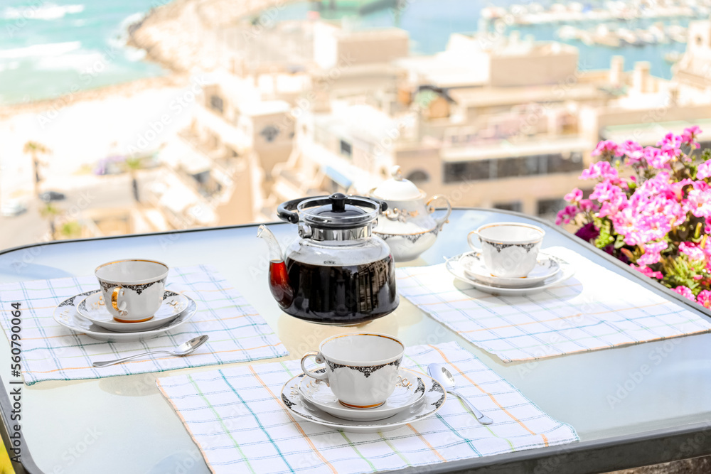 Table with coffee pot and cups near window, closeup