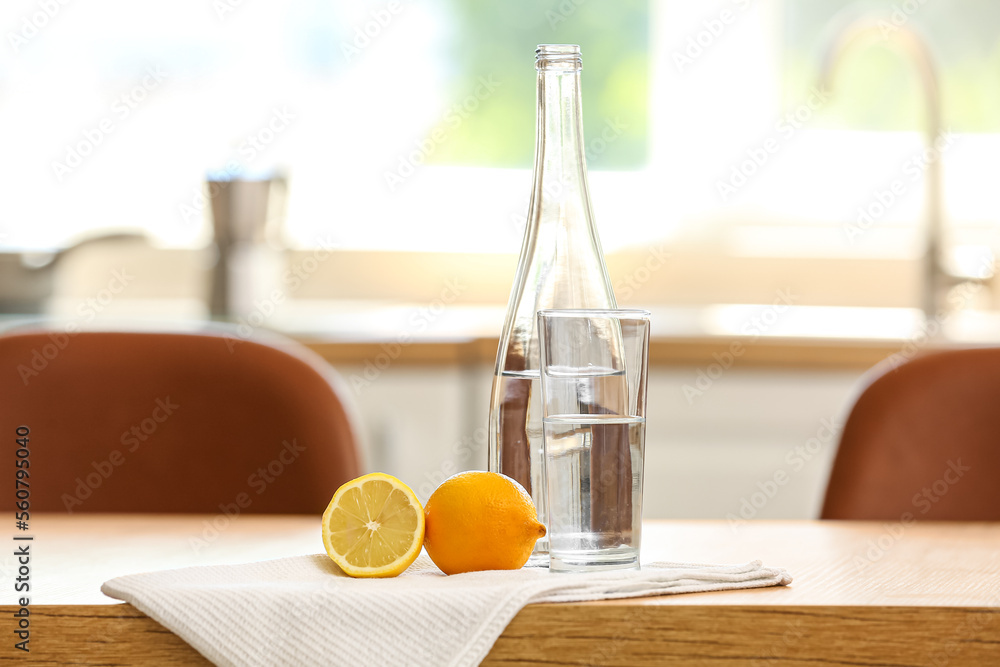 Bottle of water with glass, lemon and napkin on table in kitchen