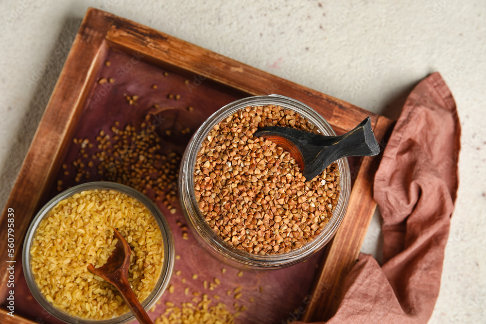 Jars with bulgur and buckwheat on light background, closeup