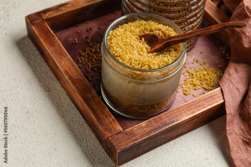 Wooden board with jar of bulgur on light background, closeup