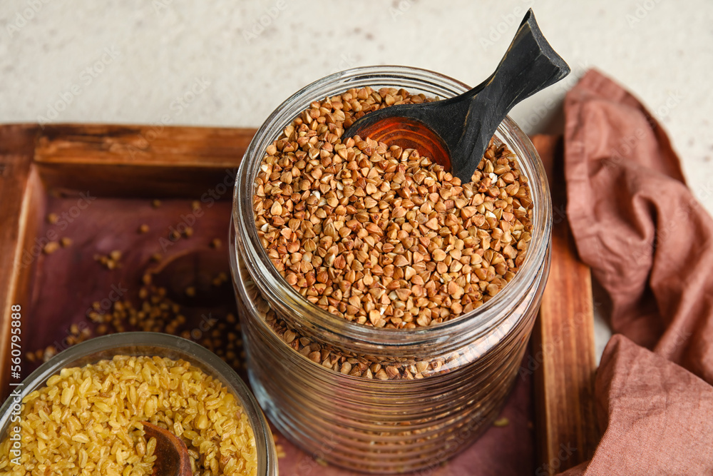 Wooden board with jar of buckwheat on table, closeup