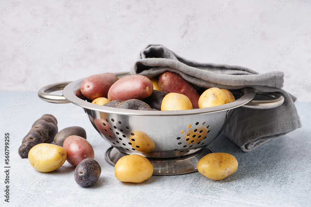 Colander with different raw potatoes on light background