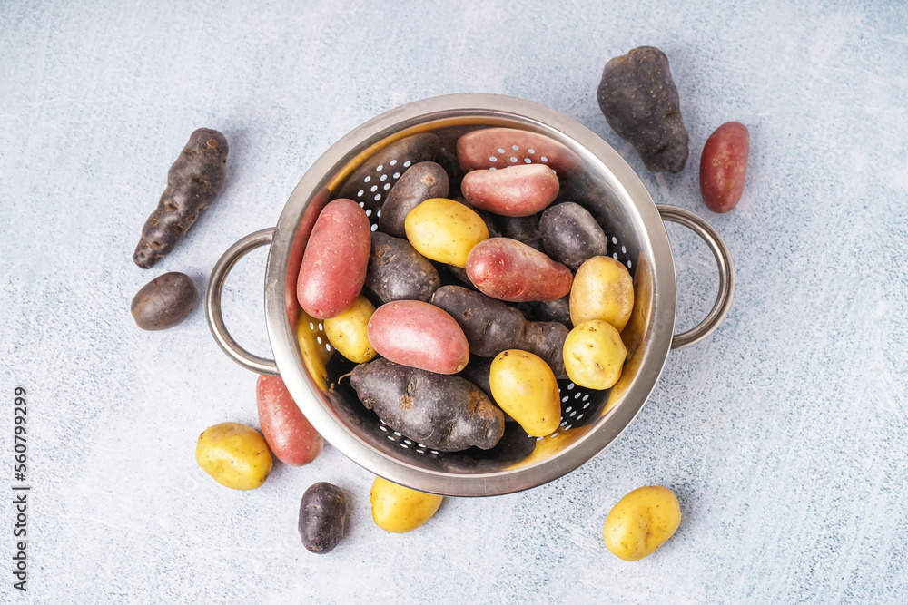 Colander with different raw potatoes on light background