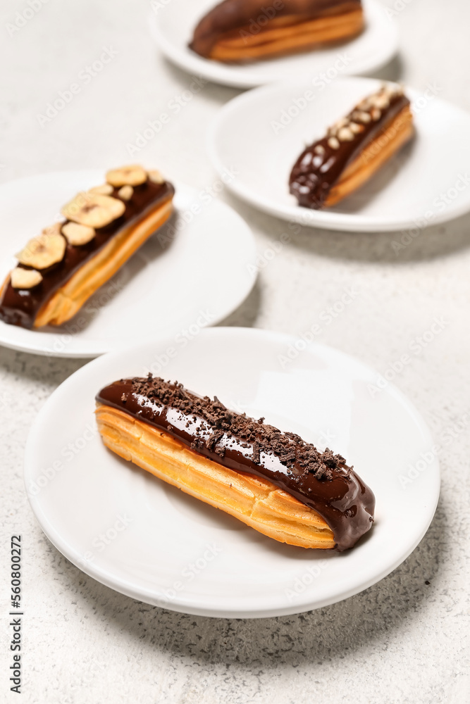 Plates with tasty chocolate eclairs on light background, closeup