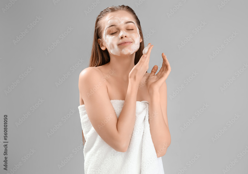 Beautiful young woman with soap foam on face against grey background