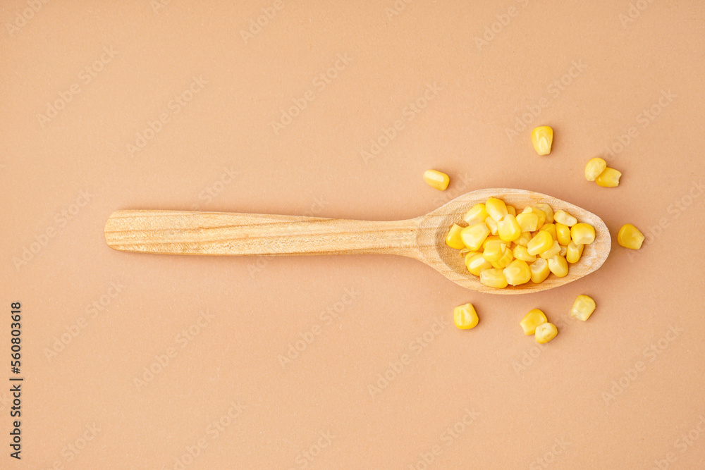 Wooden spoon with canned corn kernels on beige background