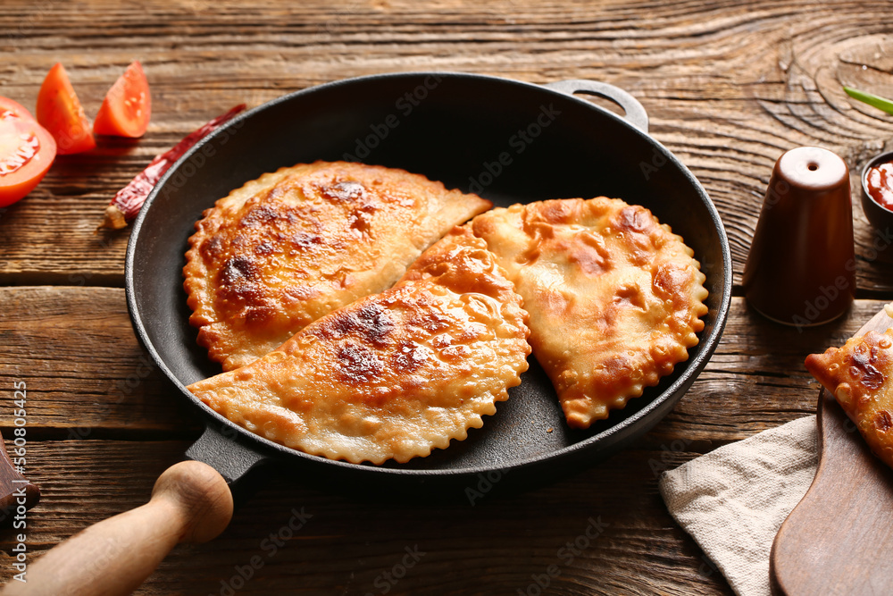 Frying pan with tasty chebureks on wooden background