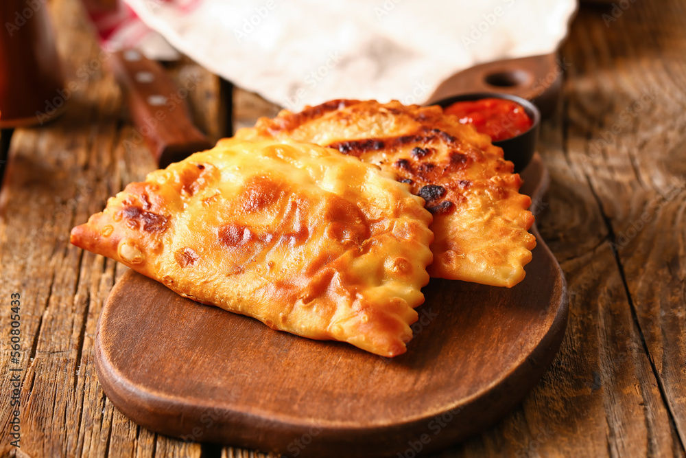 Cutting board with tasty chebureks on wooden background