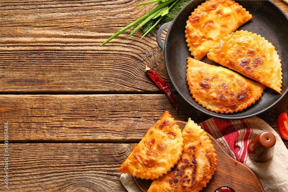 Frying pan and board with tasty chebureks on wooden background