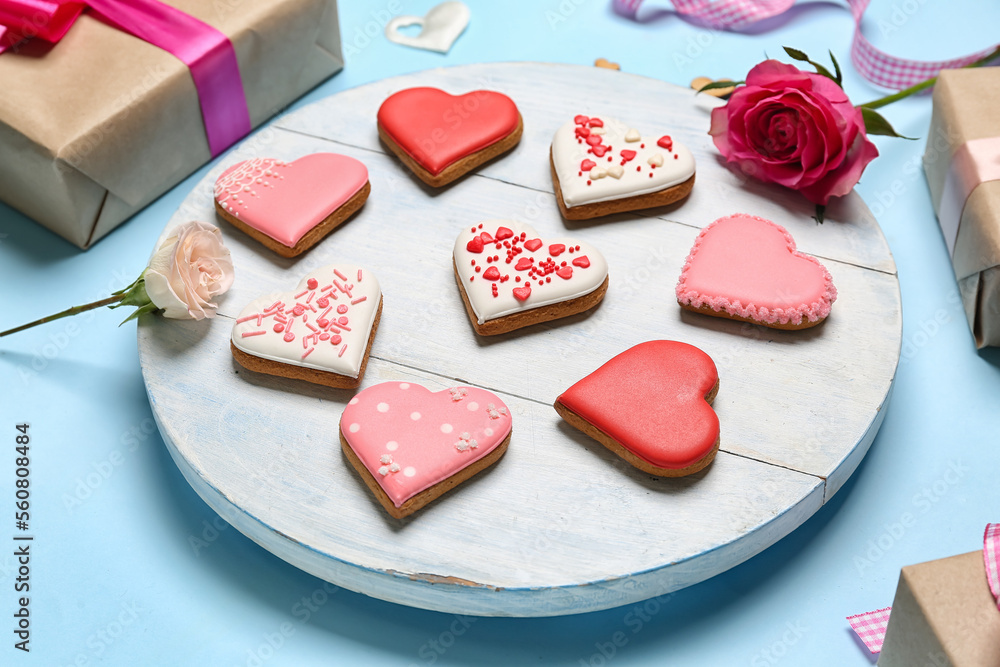 Wooden board with tasty heart shaped cookies and rose flowers on color background, closeup. Valentin