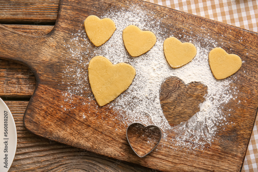 Wooden board with raw heart shaped cookies and cutter on wooden background, closeup. Valentines Day 