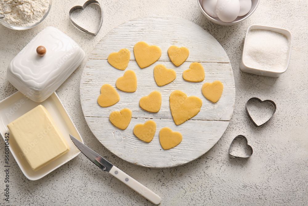 Wooden board with raw heart shaped cookies, ingredients and cutters on light background. Valentines 