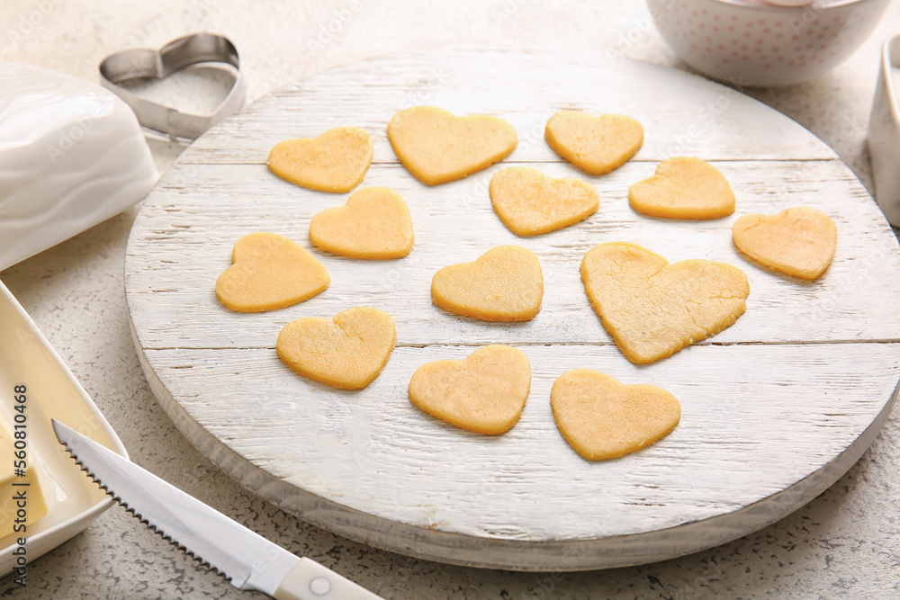 Wooden board with raw heart shaped cookies on light table, closeup. Valentines Day celebration