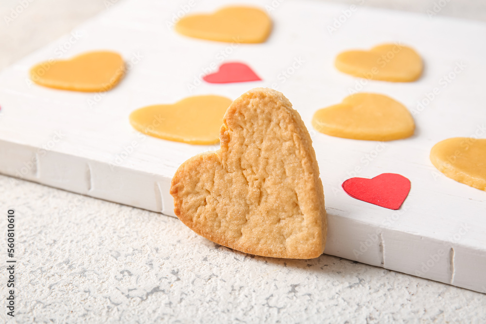 Sweet heart shaped cookie and board with raw ones on light table, closeup. Valentines Day celebratio