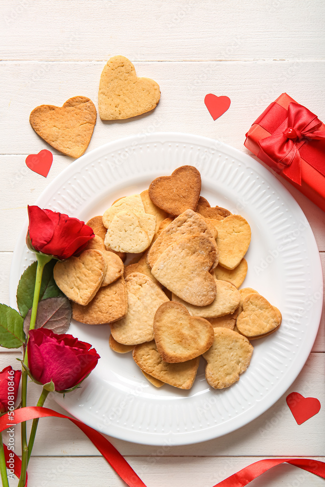 Plate of tasty heart shaped cookies and rose flowers on light wooden background. Valentines Day cele